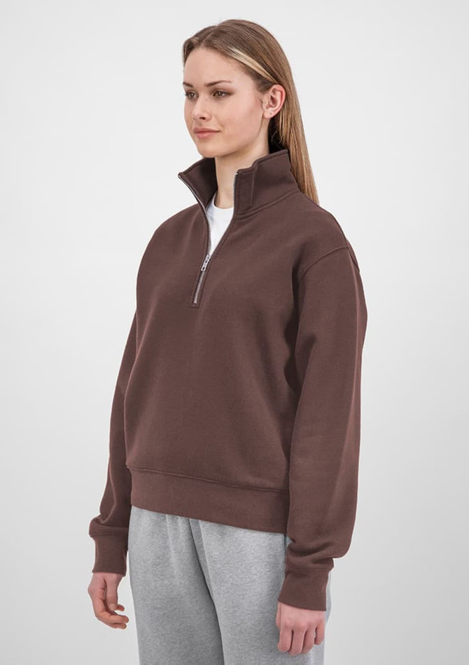 A brown women's 1/4 zip jumper is displayed on a model, paired with grey pants and featuring a branded logo.