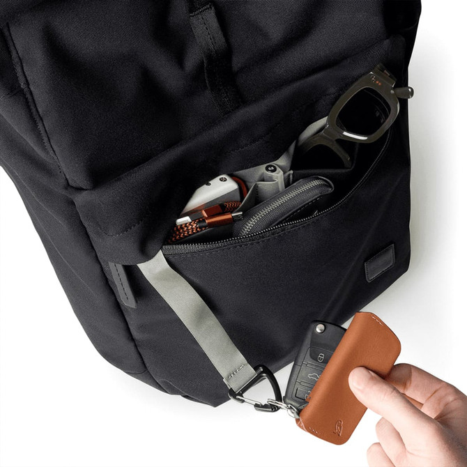 A black backpack with a front pocket containing accessories and a hand holding a brown wallet.