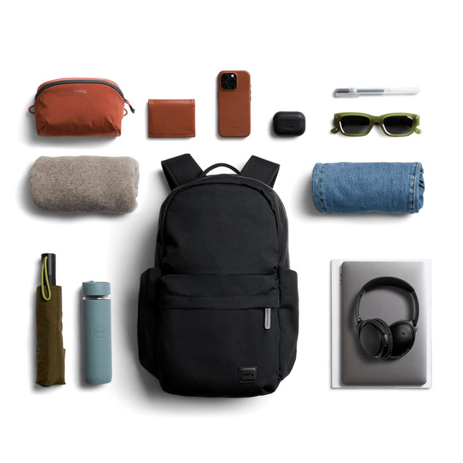 A black backpack surrounded by a drink bottle, sunglasses, a blanket, denim, headphones, and other accessories.