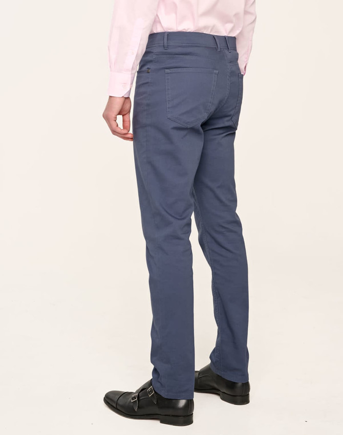 Men's blue jean style flexi chino pants displayed from the back, paired with a light pink shirt and black shoes.