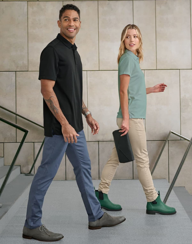 A pair of models walking, wearing black and mint polo shirts, with tan flexi chino pants, and green boots.