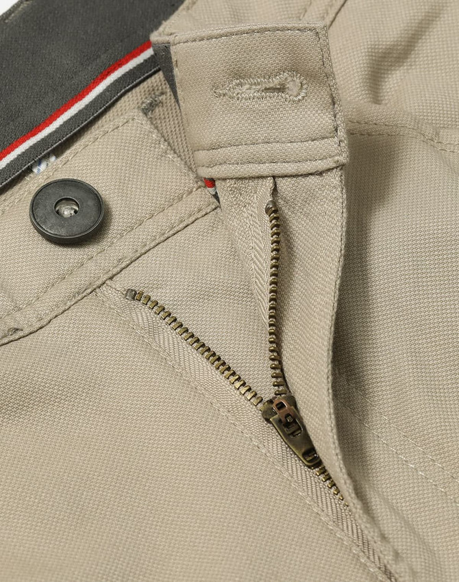 A close-up of beige chino pants featuring a zipper, button, and waistband details. The fabric has a textured finish.