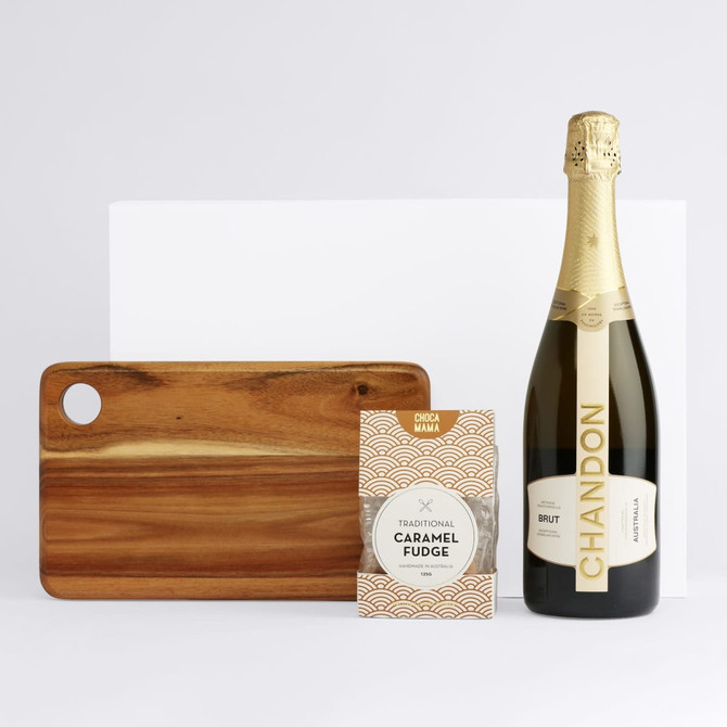 A drink bottle of sparkling wine, a packet of caramel fudge, and a wooden serving board. The wine bottle features branding.