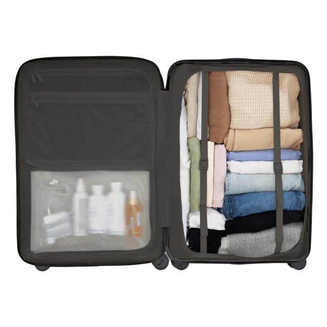 A large dark grey suitcase with packed clothes and a clear pocket containing toiletries and a mask.