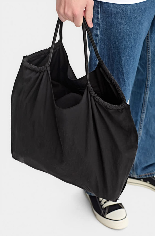 A black nylon tote bag with two compartments, being held by a person in casual attire.