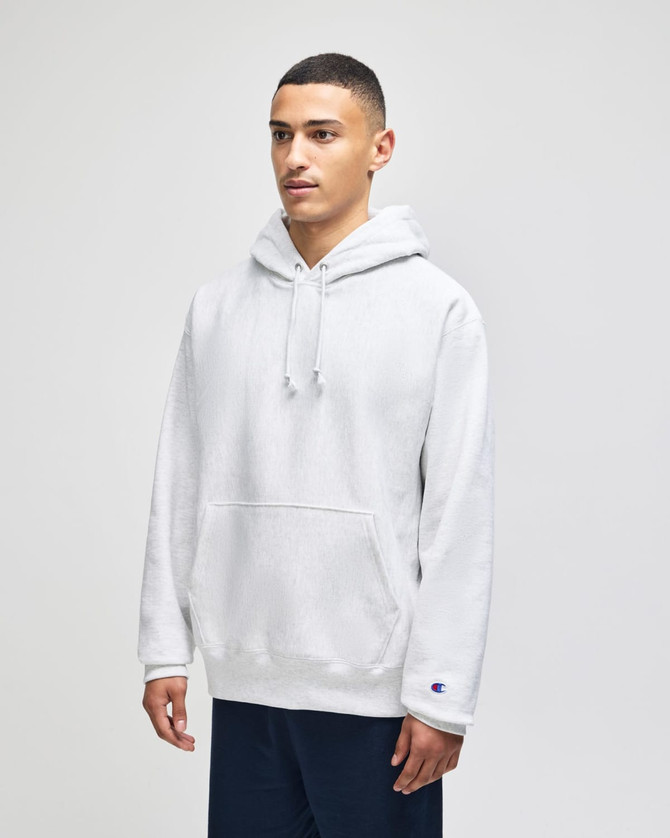 A white pullover hooded sweatshirt with a front pocket and a logo on the sleeve, worn by a model.