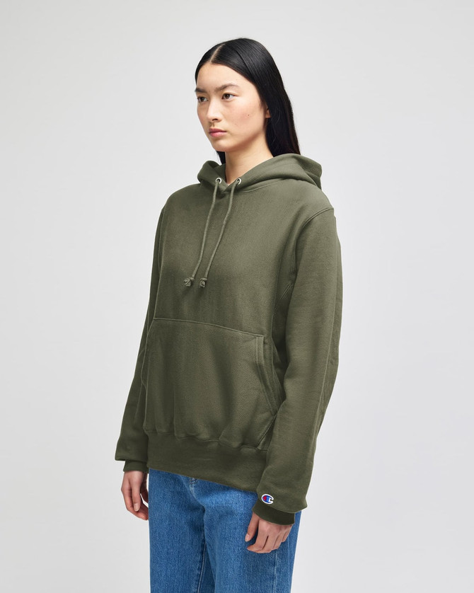 A green hooded sweatshirt with a front pocket and a logo on the sleeve, worn by a model.