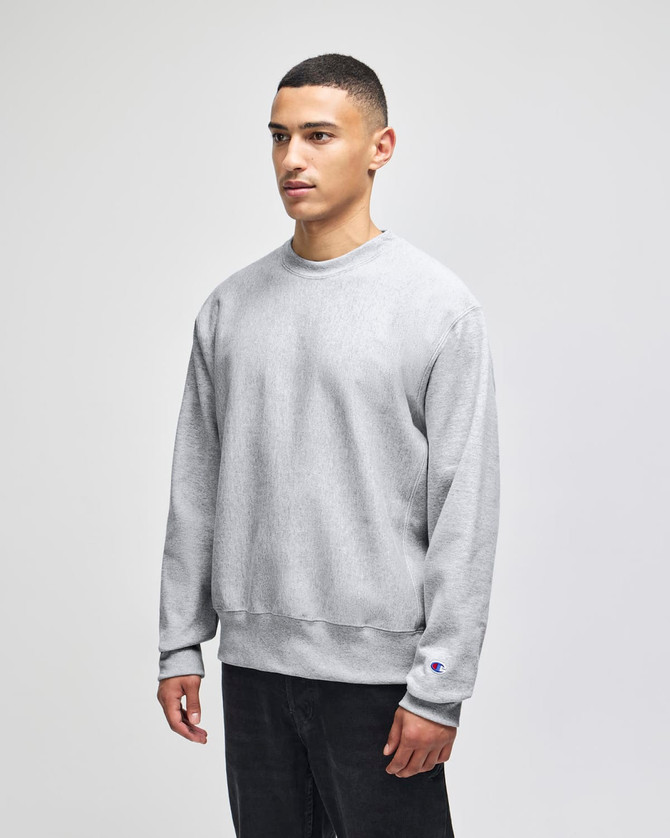 A grey Champion Reverse Weave® adult crew sweatshirt on a model, featuring a branding logo on the sleeve.