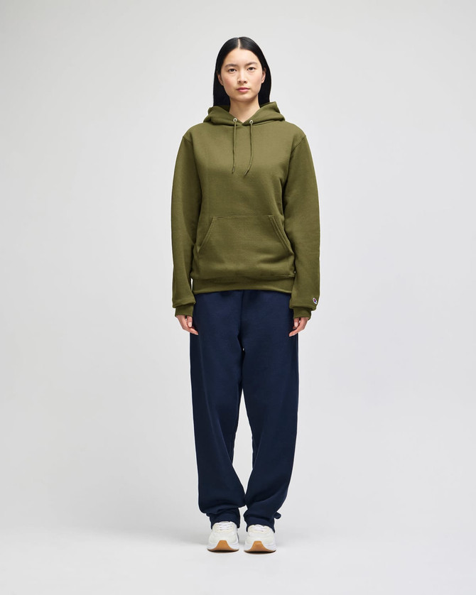 An adult pullover hooded sweatshirt in olive green, worn with navy trousers, featuring a logo.