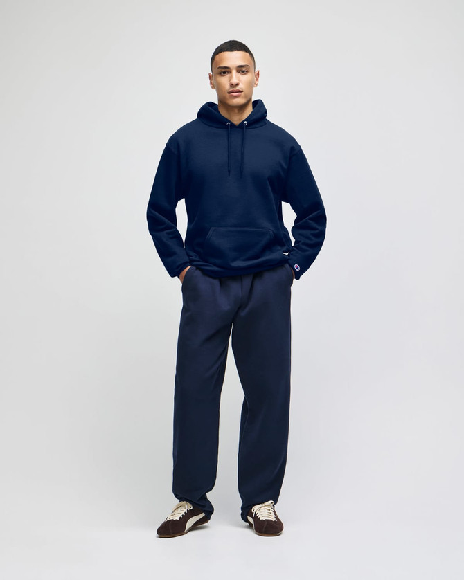 A navy blue pullover hooded sweatshirt on a model, paired with matching navy pants. The sweatshirt features a logo.