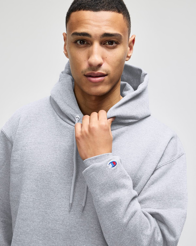 A grey hooded sweatshirt with a front pocket and a logo on the sleeve, modelled by a person.