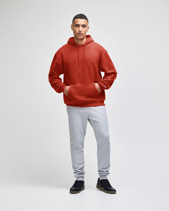 A man wearing a red pullover hooded sweatshirt and grey sweatpants, standing against a plain background.
