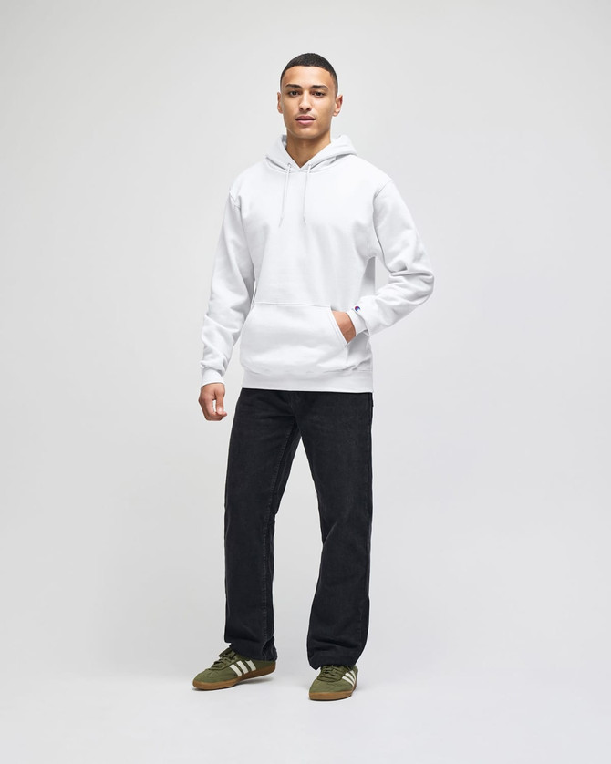 A white pullover hooded sweatshirt worn with dark jeans and trainers, featuring a logo on the garment.