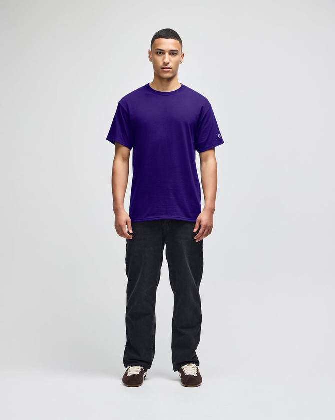 A purple short-sleeve t-shirt worn by a model, paired with black pants. The shirt features a logo.