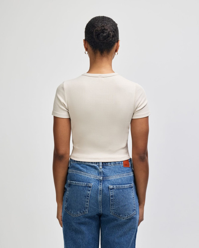A fitted beige crop t-shirt with short sleeves, displayed from the back, paired with high-waisted jeans.