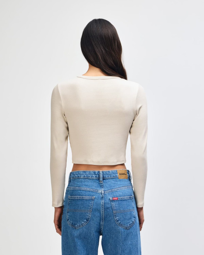 A fitted women's long-sleeve crop t-shirt in a neutral shade, viewed from the back, paired with high-waisted jeans.