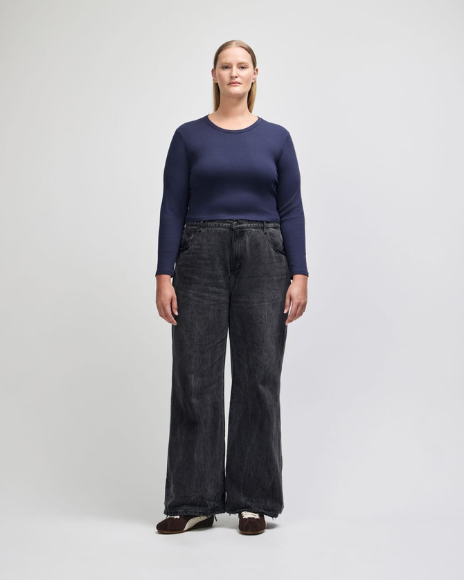 A fitted long-sleeve crop T-shirt in navy, paired with wide-leg black jeans. The model stands upright against a plain background.