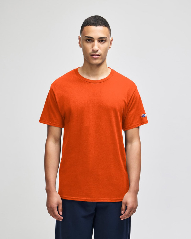 An orange Champion adult jersey short sleeve T-shirt displayed on a model, featuring a logo on one sleeve.