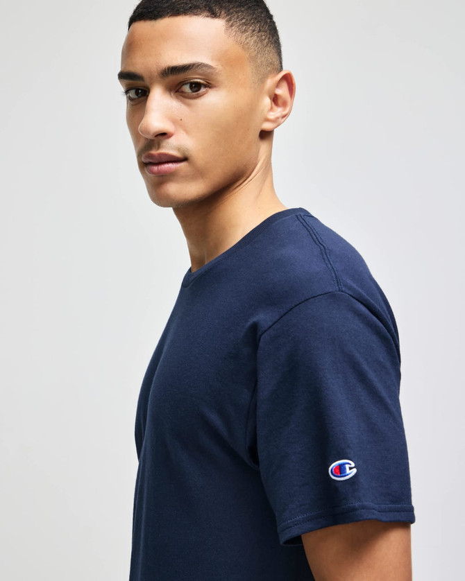 A navy short sleeve t-shirt featuring a logo on the sleeve. The model is facing sideways.