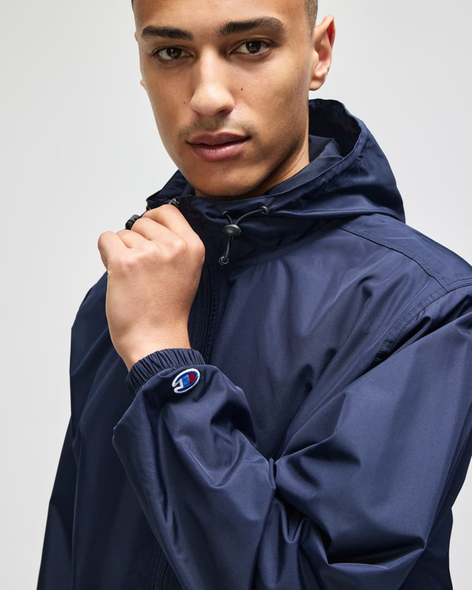 A navy full-zip anorak jacket with a hood, featuring an emblem on the sleeve.