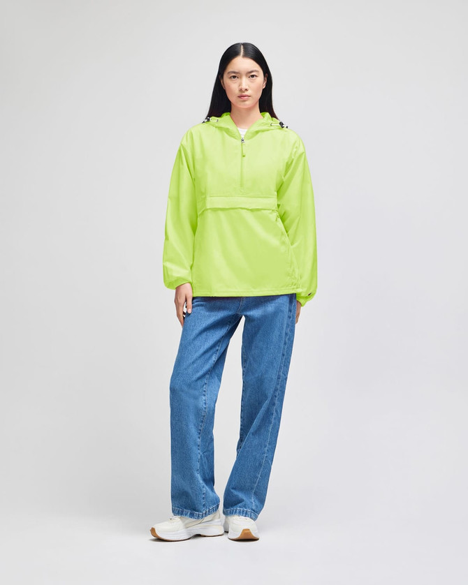 A bright lime green packable anorak jacket with a hood, worn with blue jeans. The model also wears white shoes.