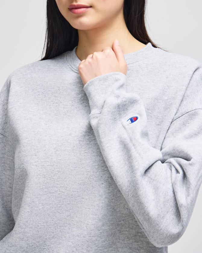 A grey sweatshirt with a crewneck design, featuring a logo on the sleeve.