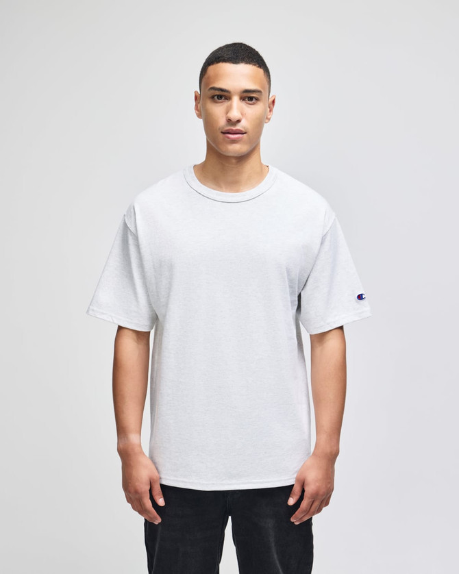 A grey Champion Adult Heritage Jersey T-Shirt displayed on a male model against a plain background.