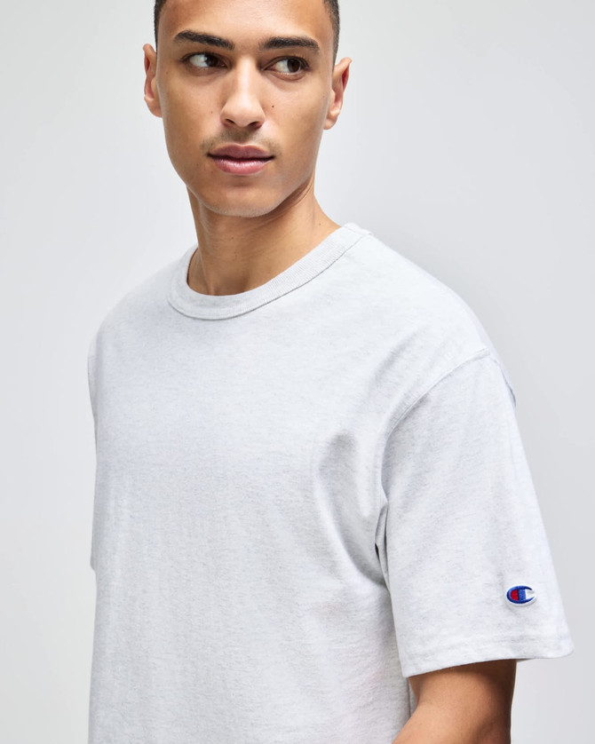 A light grey t-shirt displayed on a model, featuring a logo on the sleeve. Simple and classic design.