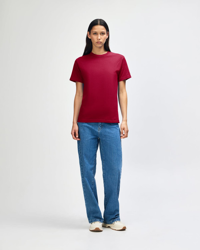A model wearing a heavyweight cotton unisex T-shirt in burgundy, paired with blue jeans.