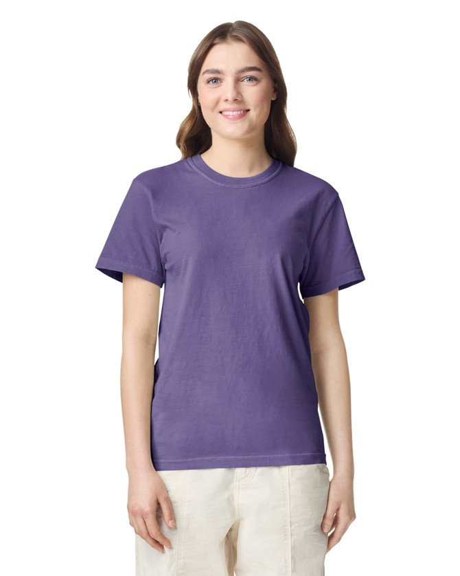 A woman is wearing a purple heavyweight T-shirt. The shirt has a logo and is styled with a relaxed fit.