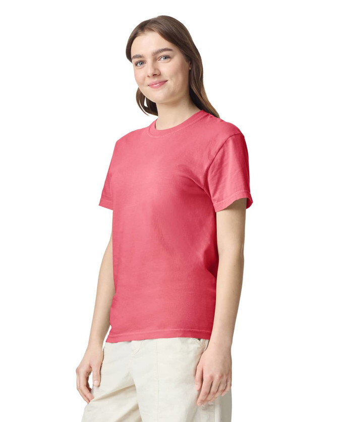 A woman wearing a coral heavy T-shirt, standing with a slight smile, featuring a logo on the shirt.