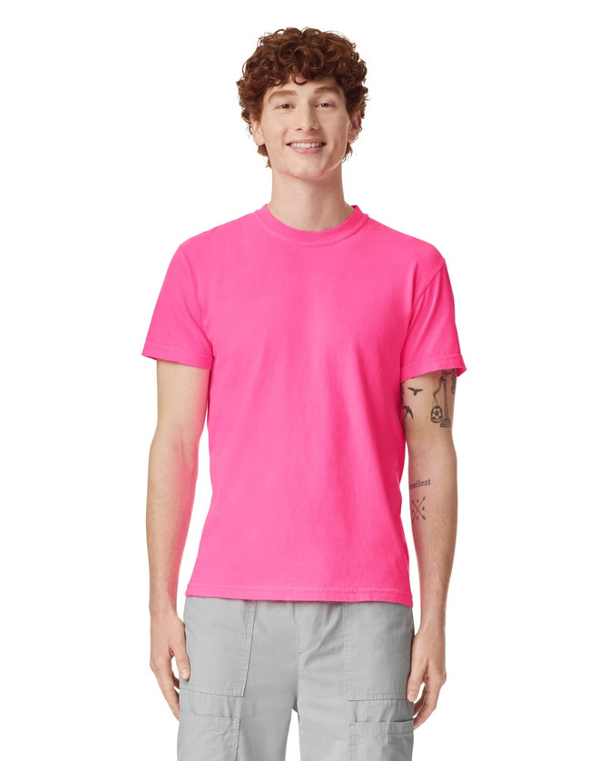 A bright pink adult heavyweight T-shirt displayed on a smiling male model, featuring short sleeves and a casual fit.