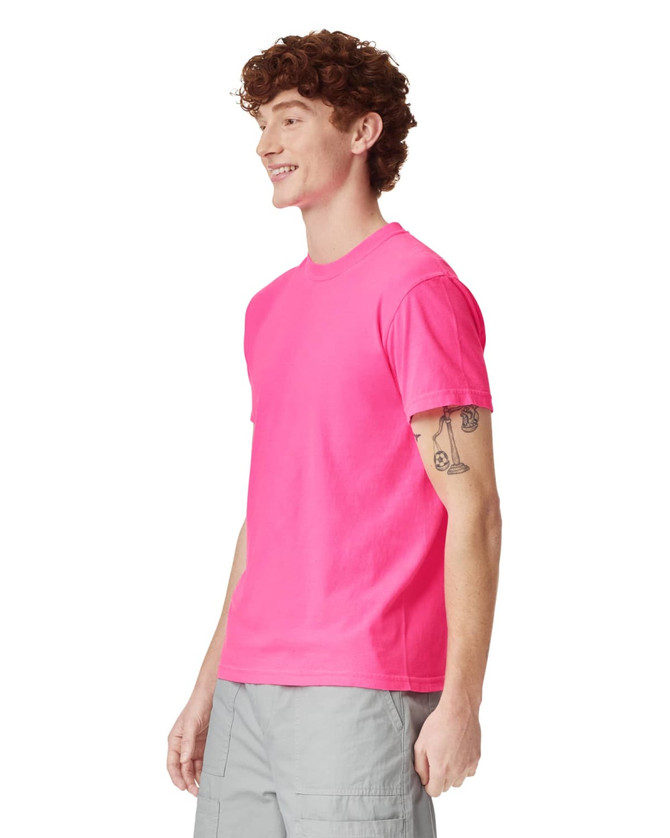 A vibrant pink heavyweight t-shirt displayed on a smiling model, featuring a simple design and a logo.
