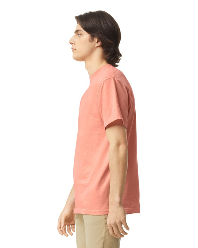 A side view of an adult heavyweight t-shirt in coral colour, featuring a simple design and a logo.