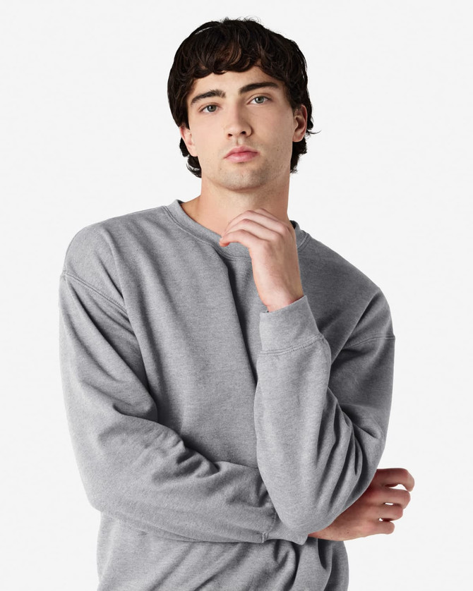A grey Gildan Heavy Blend adult crewneck sweatshirt displayed on a model posing thoughtfully. It features a logo.