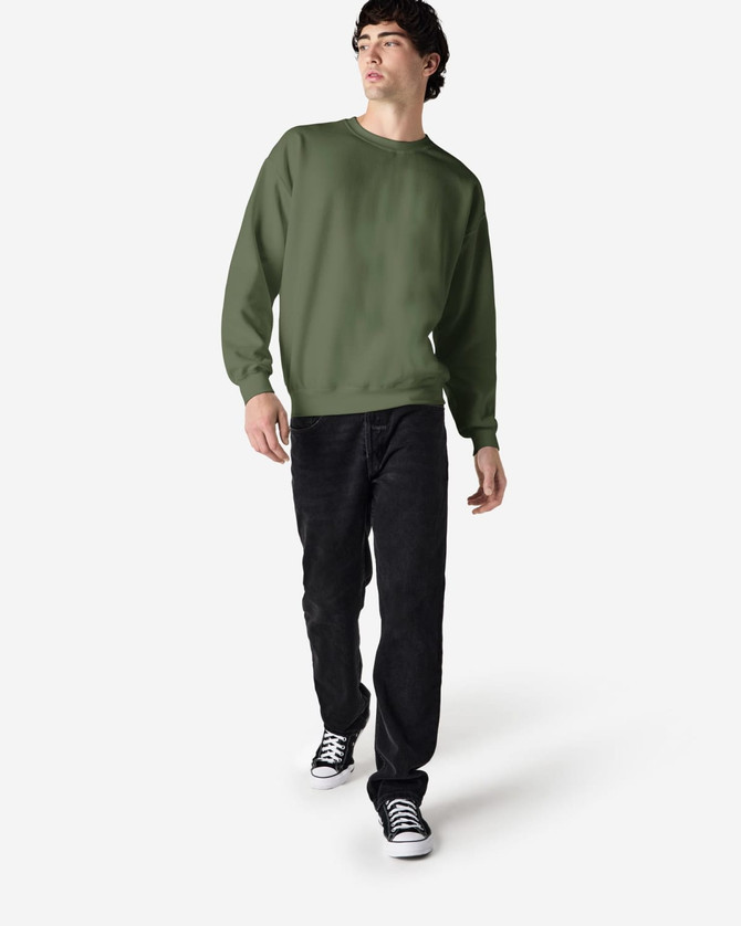 An olive green crewneck sweatshirt worn by a model, paired with black pants and sneakers. It has a logo on the sweatshirt.