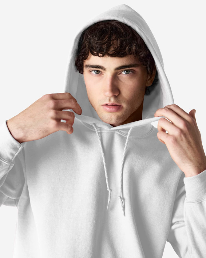 A white Gildan Heavy Blend adult hooded sweatshirt is worn by a young man adjusting the hood. The product features a logo.
