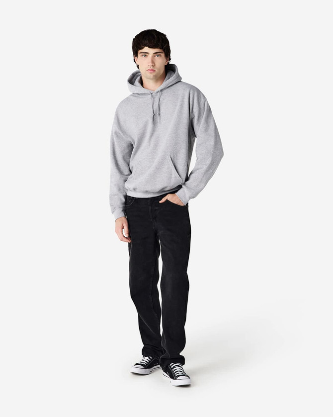 A grey hooded sweatshirt is worn by a male model, paired with black jeans and sneakers. The sweatshirt has a logo.