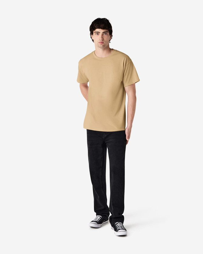 A male model wearing a plain beige Gildan Ultra Cotton adult t-shirt paired with black pants and Converse shoes.