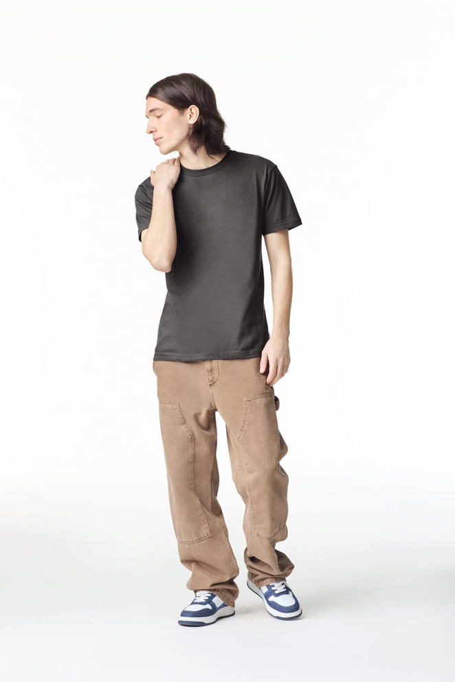 A unisex fine jersey short sleeve t-shirt in black, worn with beige pants and blue sneakers, with a logo visible.