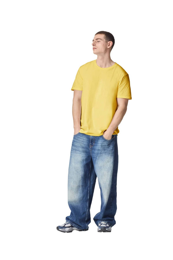 A model wearing a yellow unisex fine jersey short sleeve t-shirt and loose blue denim jeans, hands in pockets.