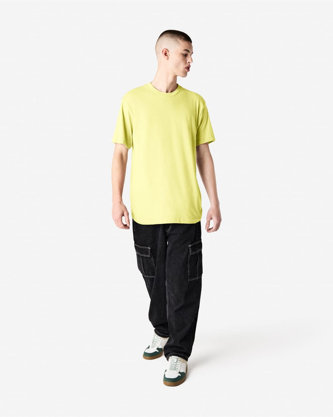 A man wearing a bright yellow unisex short sleeve t-shirt and black baggy pants, with sneakers.