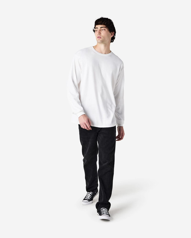 A white long sleeve T-shirt worn by a man, paired with black pants and shoes, standing against a light background.