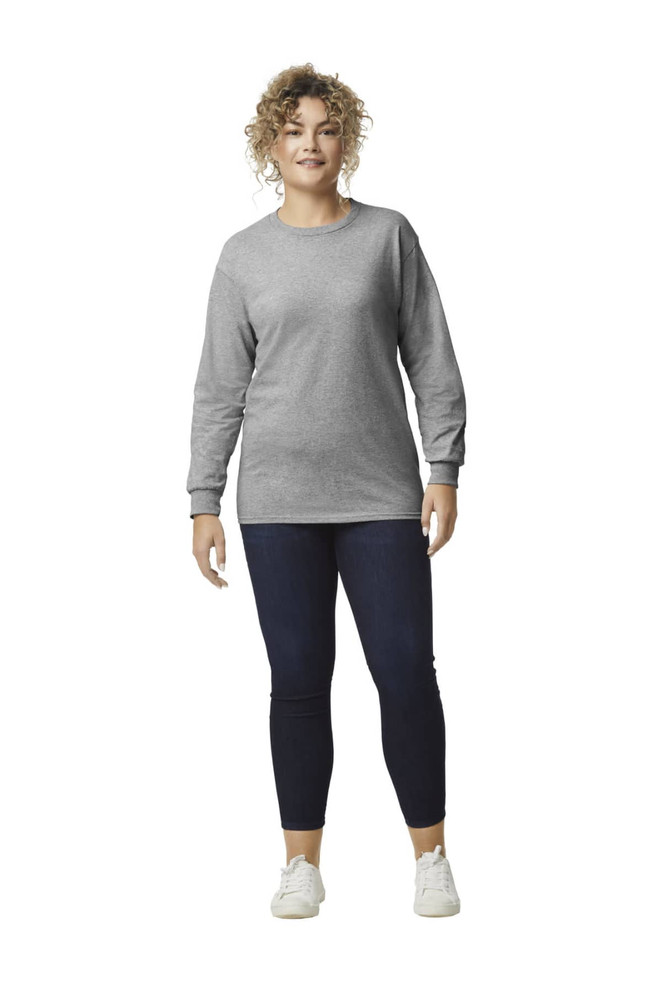 A woman stands wearing a grey long sleeve T-shirt and navy leggings, with a logo visible on the shirt.