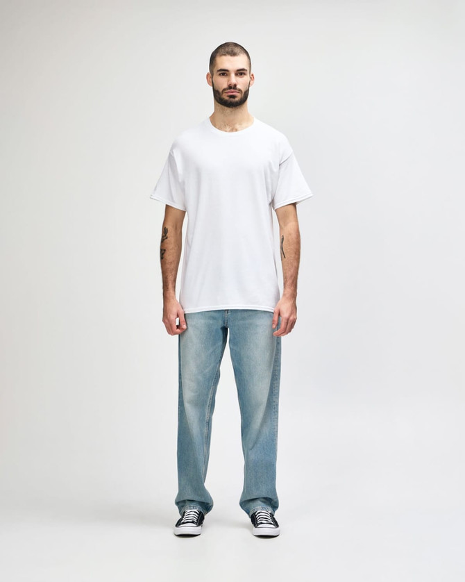 A man in a plain white Gildan Heavy Cotton T-shirt paired with blue jeans and black shoes, standing against a neutral background.