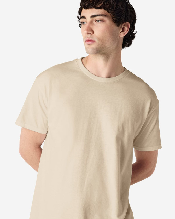 A beige Gildan Heavy Cotton Adult T-Shirt on a model, featuring a round neckline and a logo.