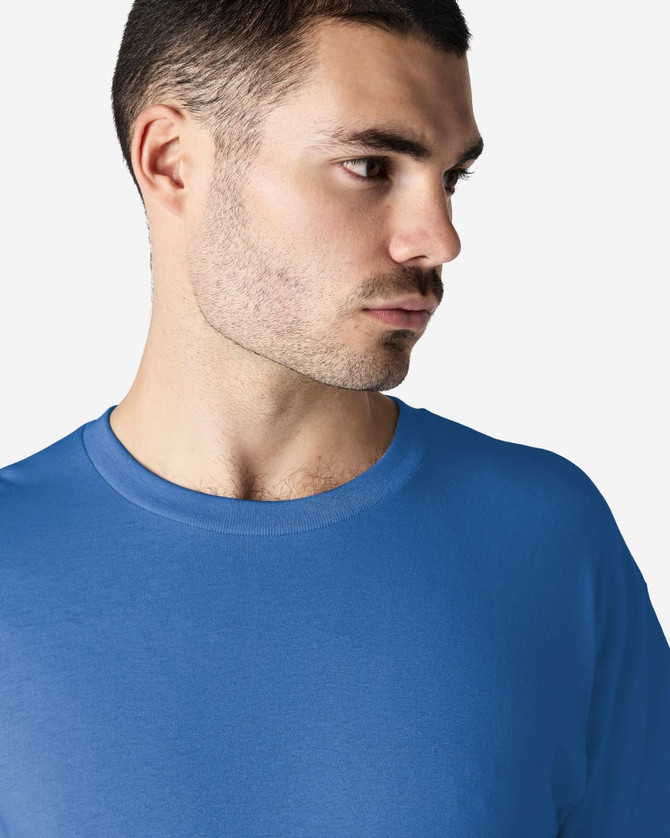 A man wearing a blue Gildan Heavy Cotton Adult T-Shirt. The shirt features a crew neckline and has a logo.