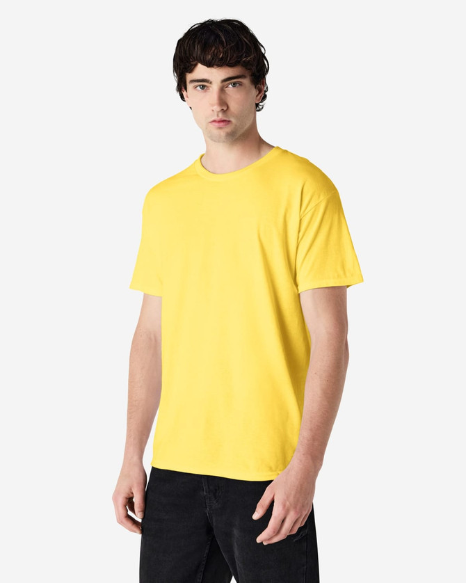 A yellow Gildan Heavy Cotton Adult T-Shirt on a model, featuring a logo. The shirt has a classic fit and short sleeves.