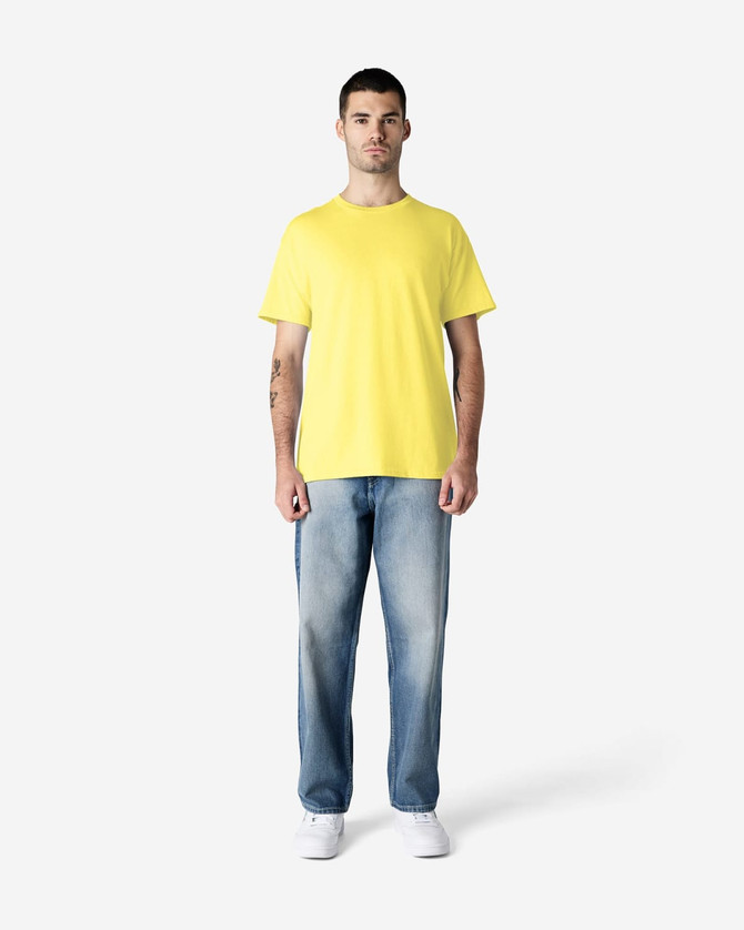 A man wearing a bright yellow Gildan Heavy Cotton adult T-shirt paired with blue jeans. The shirt has a logo.