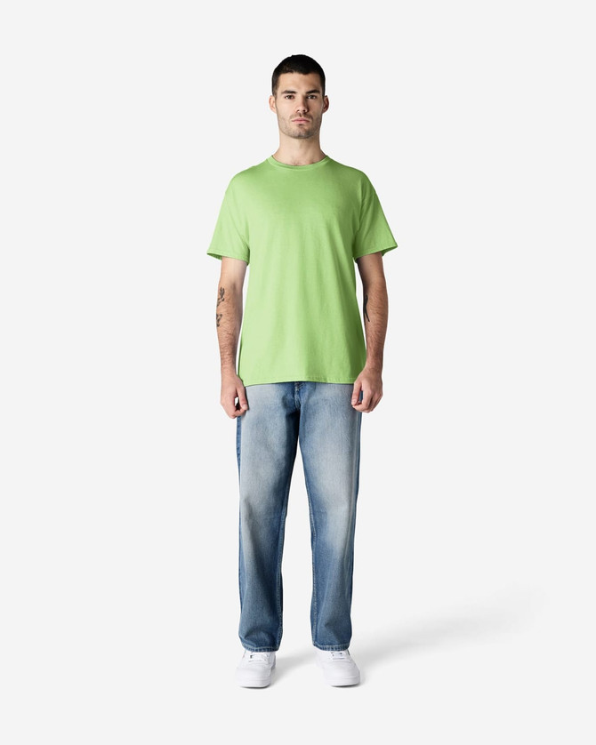 A man stands wearing a bright green Gildan Heavy Cotton adult T-shirt and black jeans, with a logo on the shirt.